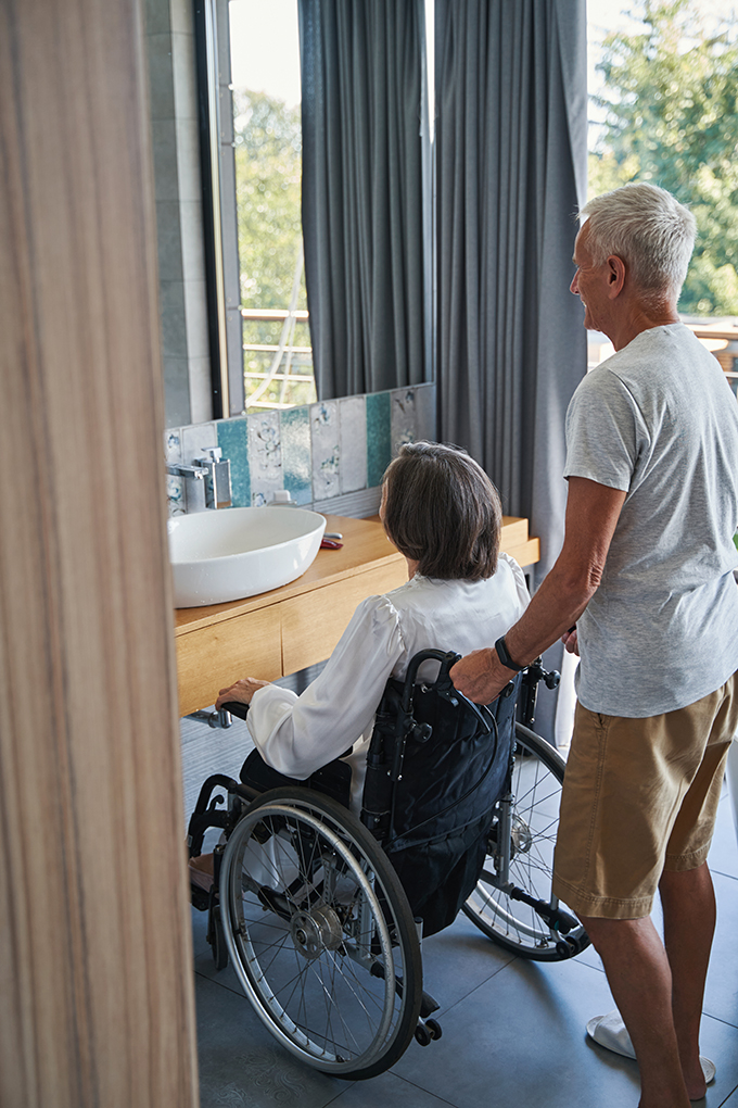 aging male holding wheelchair of disabled person from behind